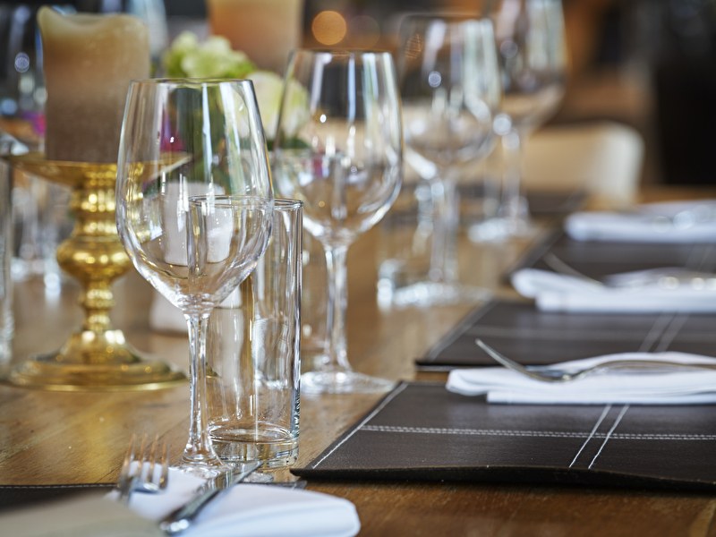 Set dining table with wine glasses, water glasses, cutlery, and black-and-white placemats with a golden candlestick.